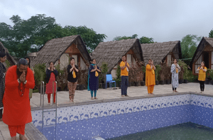 Group meditation outdoors beside a pool and cottages