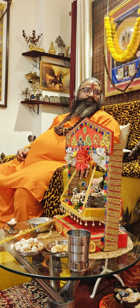 Tantrguru Shree Ganesh Dubey seated beside the decorated Laddu Gopal jhula with diya and bhog on Janmashtami