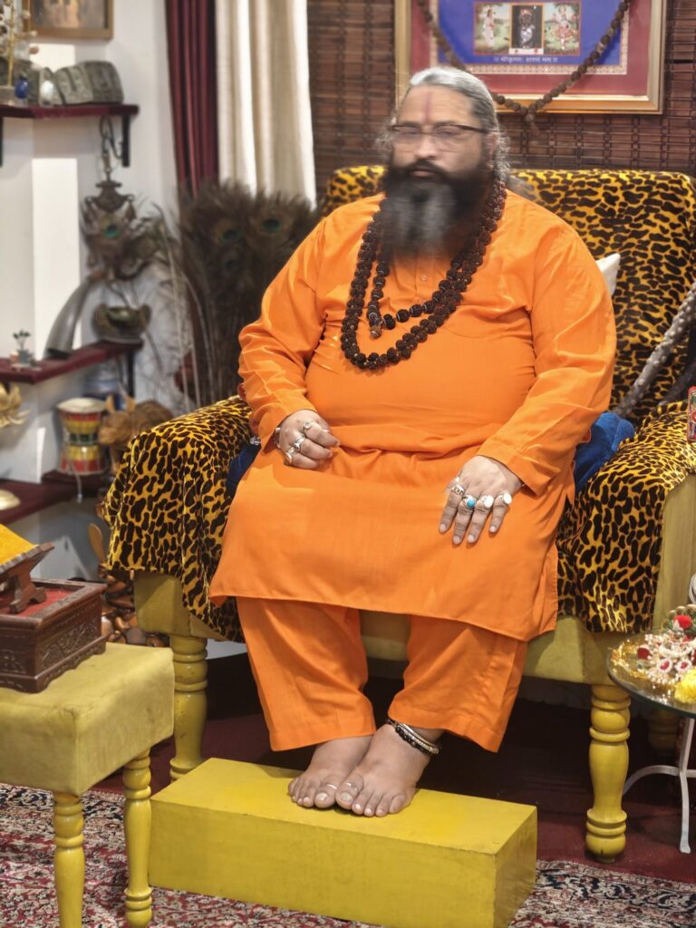 Tantrguru Shree Ganesh Dubey seated in saffron robes during the Janmashtami celebration